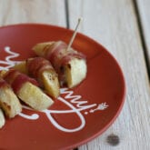 Pumpkin spice baked apple slices wrapped in bacon on an orange plate.