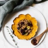 A plate with a stuffed acorn squash and a wooden spoon next to it.