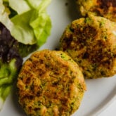 A white plate with a few salmon cakes next to lettuce.