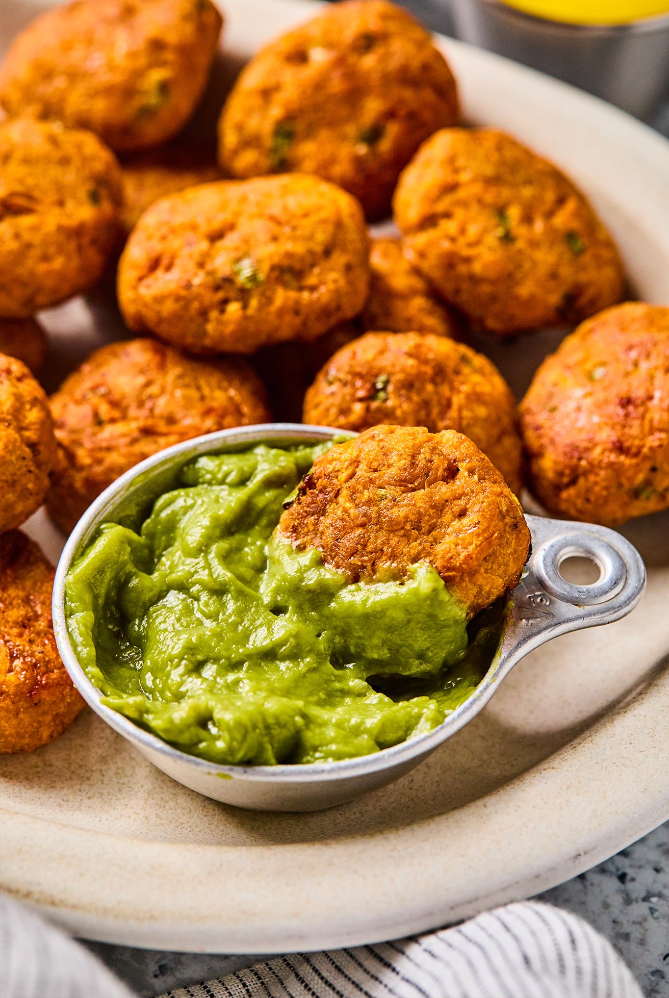 Sweet potato chicken poppers on a plate with one dipping into a bowl of guacamole. 