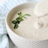 A bowl of garlic cream sauce with a spoon taking a spoonful out.