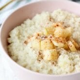 A pink bowl filled with cauliflower oats topped with cinnamon and apples.