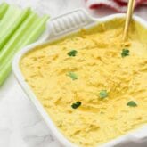 A white ceramic dish filled with buffalo chicken dip and a spoon in it and some celery next to it.
