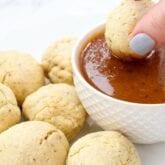 A hand dipping a pizza bite into red dipping sauce with other pizza bites next to the dipping sauce.