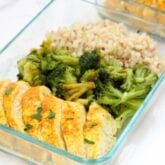 A glass meal prep container filled with turmeric chicken, cauliflower rice, and roasted broccoli.