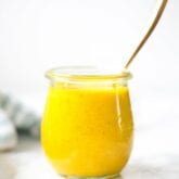 A class jar filled with turmeric dressing and a spoon sticking out of it.