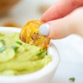 A plantain chip in a hand dipping into guacamole.