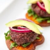 A plate with two sliders on sweet potato buns with onion and avocdo on top.