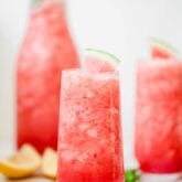 Two glasses with watermelon mocktails in them and fresh watermelon slices on top.