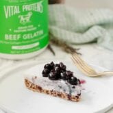 A slice of blueberry lavender cheesecake topped with blueberries on a white plate with a fork next to it.