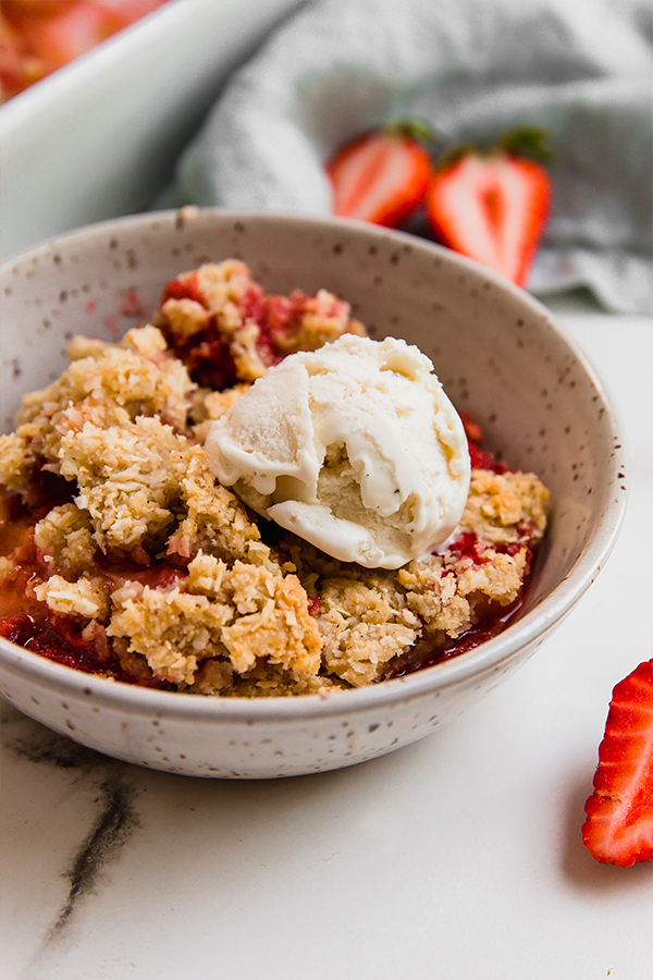 strawberry rhubarb crisp in a bowl with ice cream.