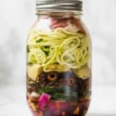 A mason jar filled with layers of onion, cucumber, olives, artichoke hearts, zucchini, and Italian dressing to make an Italian mason jar salad.