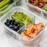 A glass meal prep container with chicken poppers, blueberries, and guacamole.
