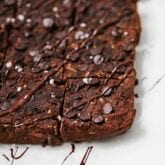 A pan of zucchini brownies cut into squares and sitting on a white counter.