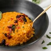 A black bowl filled with cauliflower pumpkin risotto with a spoon resting in it.