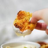 A hand holding a spaghetti squash nugget dipping into a white sauce.