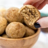 A hand taking a apple donut hole out of a wooden bowl of them.