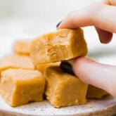 A hand taking a piece of pumpkin fudge off a stack of pumpkin fudge.