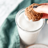 A paleo cookie being dipped into a glass of almond milk.