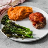 A white plate with mashed sweet potato, roasted broccolini, and slice of meatloaf on it.