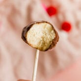 A cake pop with a bite taken out of it being held up against a fuzzy pink background.