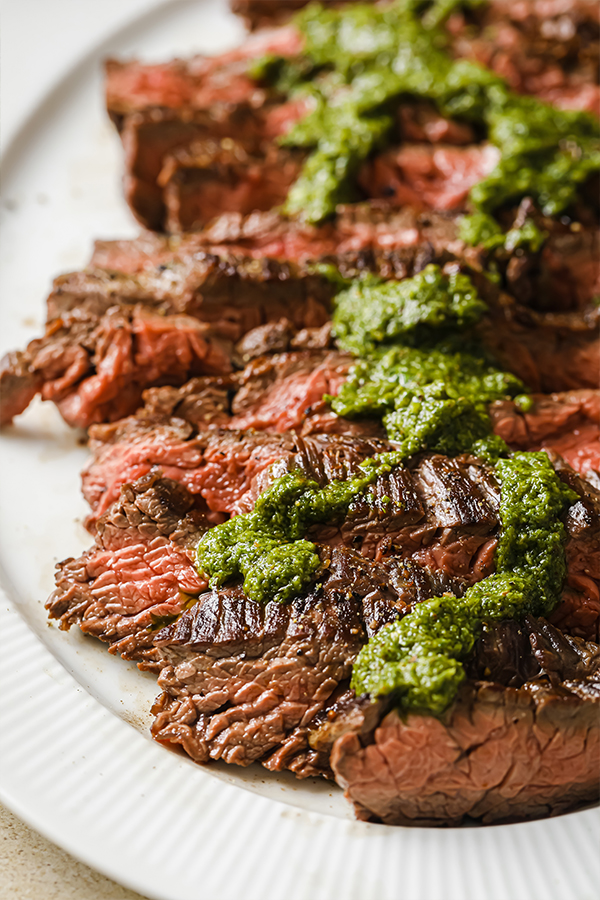 A plate of delicious looking steak with chimichurri sauce.