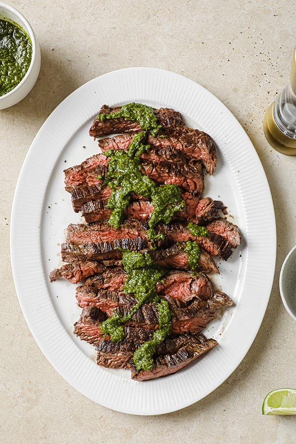 A serving plate filled with steak and chimichurri sauce.