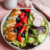 A white bowl filled with crispy chicken, berries, radish, and mixed greens to make a crispy chicken salad.