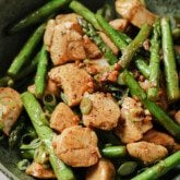 Cooked chicken and sliced asparagus in a green bowl topped with green onions