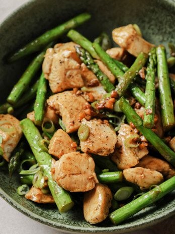 Cooked chicken and sliced asparagus in a green bowl topped with green onions