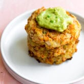 A white plate stacked with two carrot fritters topped with guacamole.