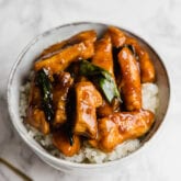 A white bowl filled with cauliflower rice topped with Mongolian chicken.
