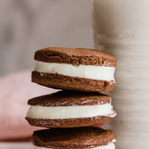 A stack of homemade oreos on top of each other next to a glass of milk.