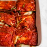 A white ceramic baking dish with layers of zucchini and sauce to make ravioli.