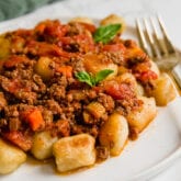 A white plate filled with gnocchi bolognese and a fork next to it.