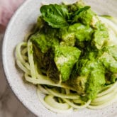 A white bowl with zoodles topped with slow cooker pesto chicken on it.
