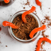 A glass jar of "dirt cup" topped with gummy worms.
