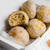 A white container filled with mandarin donut holes with a bite taken out of one of them.