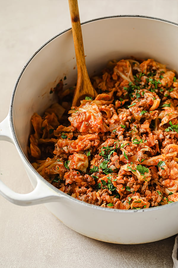 Unstuffed cabbage roll in a white pot with a wooden spoon.