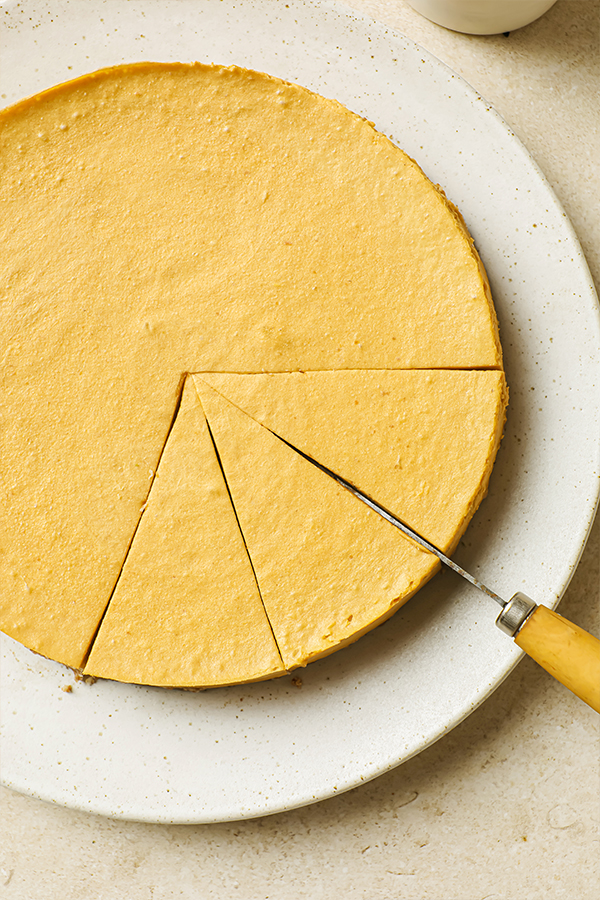 Cheesecake on a plate being cut into slices with a knife. 