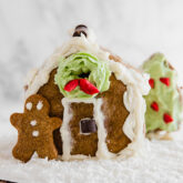A homemade gingerbread house with a gingerbread man leaning against it.