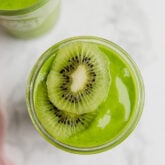 A glass filled with matcha smoothie topped with slices of fresh kiwi.