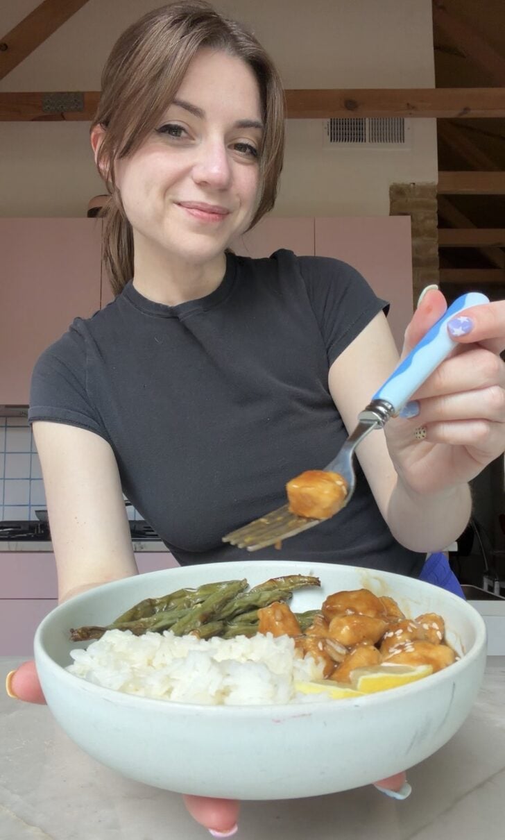 Food blogger michelle hoover with a bowl of chinese lemon chicken, with a piece of chicken on a fork