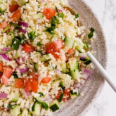 A serving bowl of cauliflower tabbouleh salad with a spoon in it.