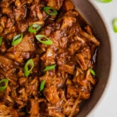 A serving bowl filled with BBQ jackfruit topped with green onions.