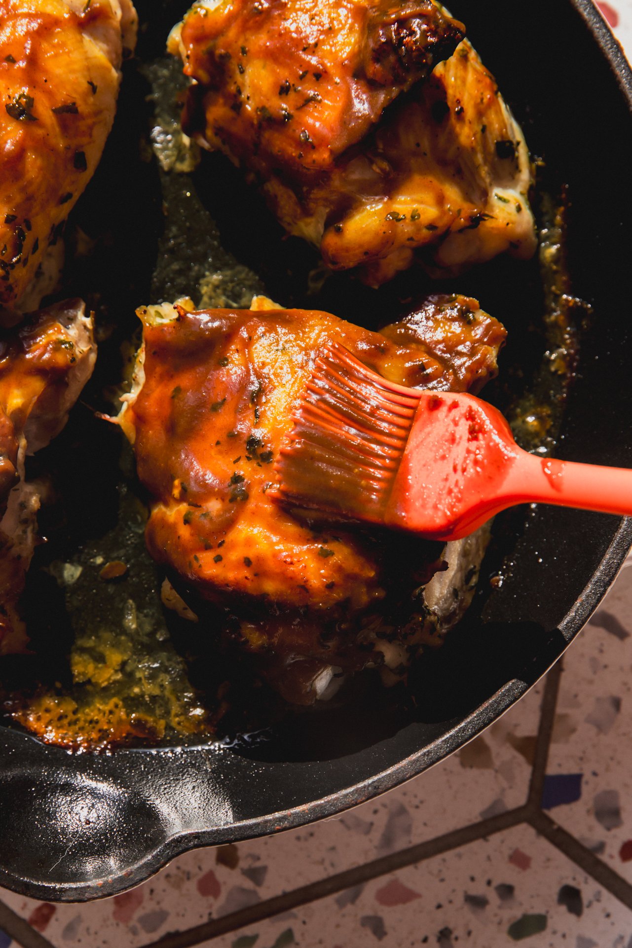 BBQ chicken in a pan with more BBQ sauce being brushed on.