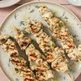 A white plate with four chicken souvlaki skewers on it.