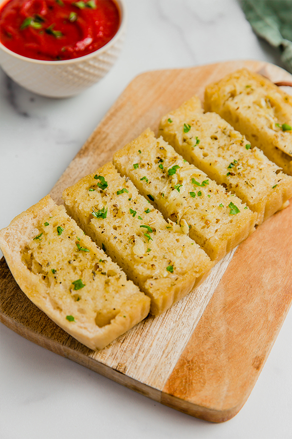 Garlic bread on cutting board with sauce on the side