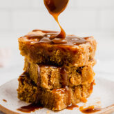 A stack of three salted caramel pumpkin blondies with caramel sauce being drizzled over it.