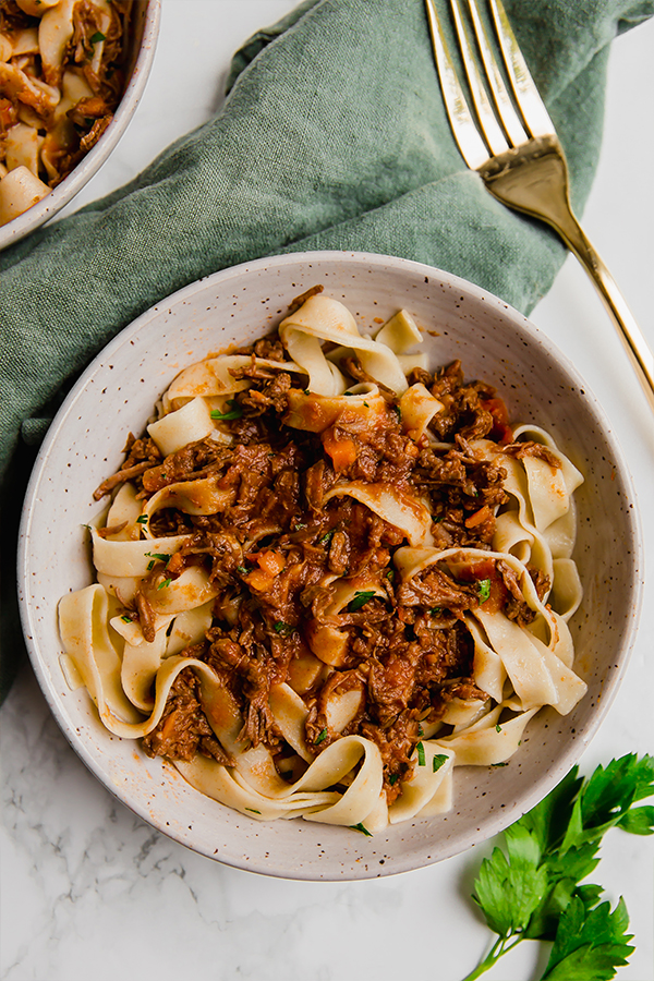 beef ragu in two bowls with green cloth and gold fork